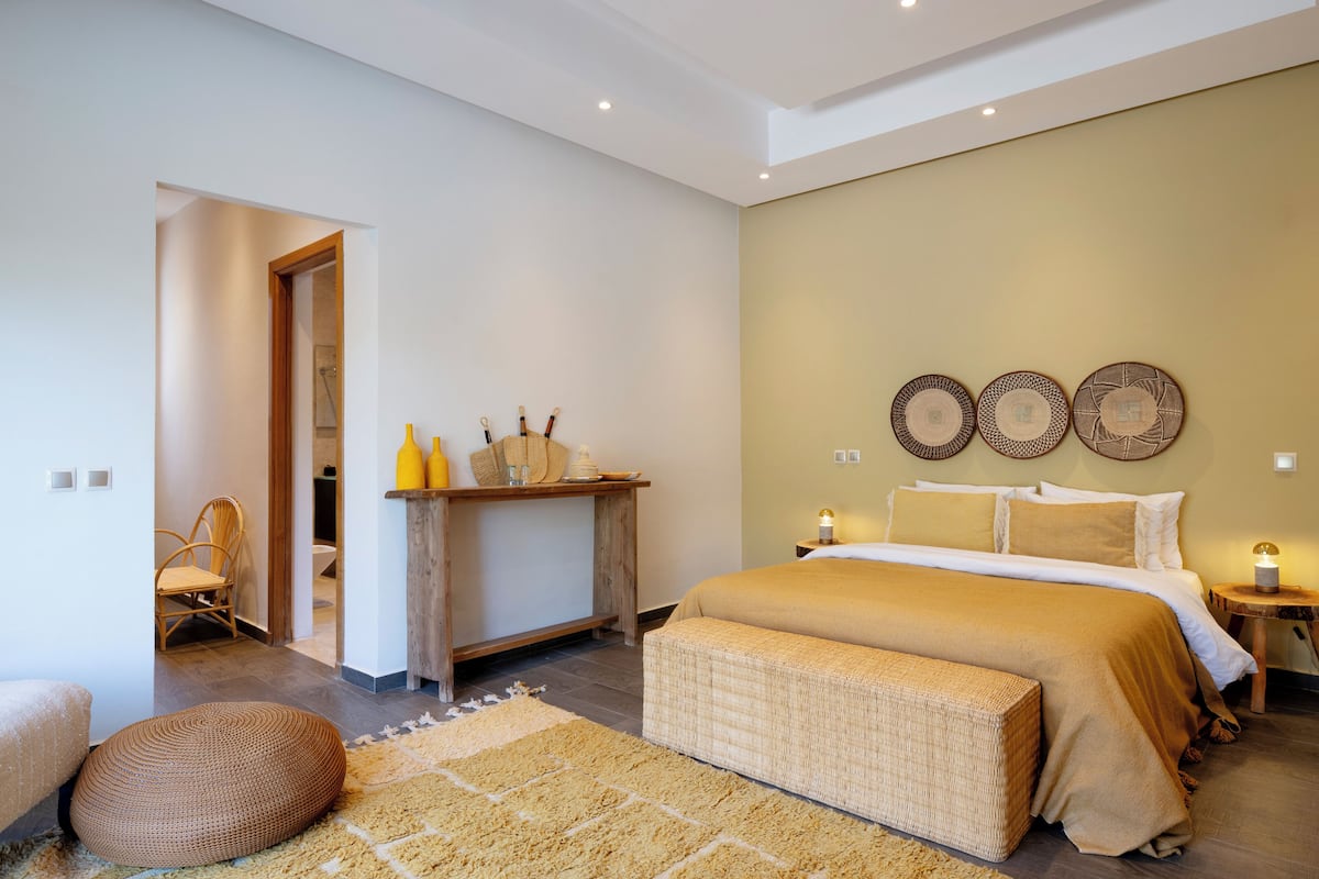 A bedroom with a bed, a bench, a chair, a bedside table, and wall decor.