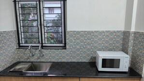 Une cuisine avec un plan de travail noir, un micro-ondes blanc, une fenêtre donnant sur un espace verdoyant et des murs recouverts de carreaux à motifs.