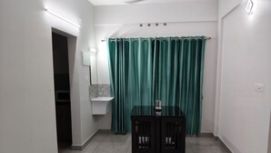Une petite pièce bien éclairée, avec un sol carrelé, une table et deux chaises, un lavabo avec un miroir et un rideau vert.