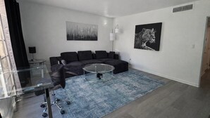 Ein modernes Wohnzimmer mit Glastisch, schwarzem Sofa und Kunstwerken an den Wänden.