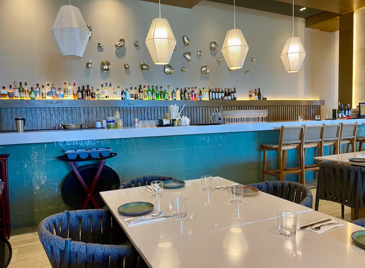 Ein Restaurant mit Barbereich, Tischen, Stühlen und hängenden Pendelleuchten.