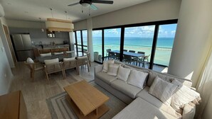 En moderne stue med en stor sofa, spisebord og stole, et køkken og en balkon med havudsigt.