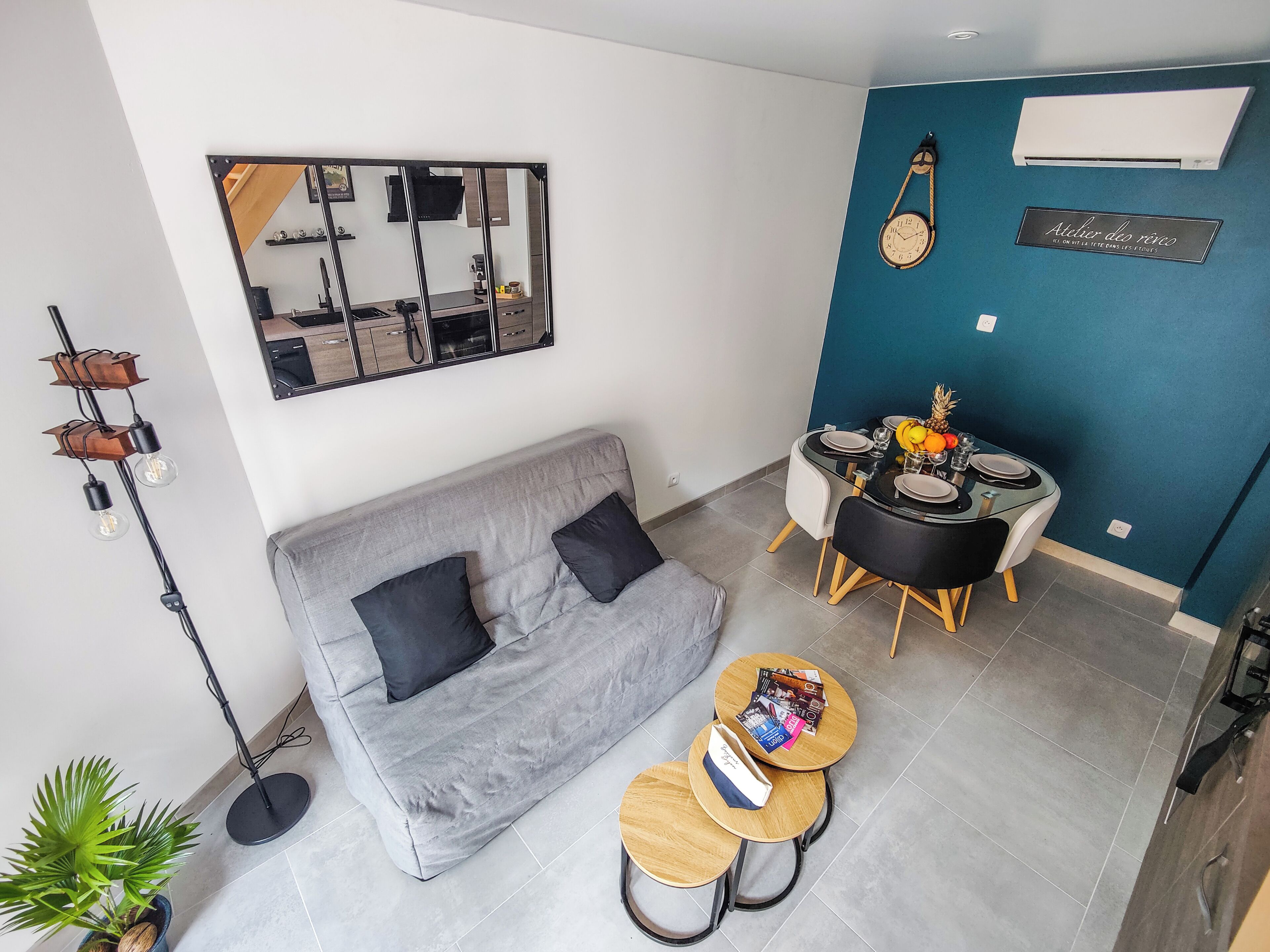 A modern living room with a grey sofa, a dining table with chairs, a small coffee table, and a wall-mounted air conditioner.