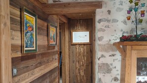 A wooden hallway with framed artwork, a stone wall, and a wooden cabinet with glass doors. - Chalet les étoiles des Alpes close to ski resorts (Saint-Jean-d'Aulps)