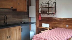 A compact kitchen with wooden cabinets, a sink, and a small refrigerator. There is a table with a checkered tablecloth and a chair. - Chalet les étoiles des Alpes close to ski resorts (Saint-Jean-d'Aulps)