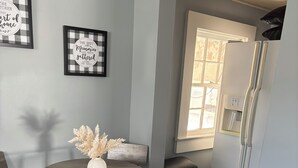 Un coin repas avec une table ronde, deux chaises, un vase contenant des fleurs séchées, un tapis en peau de vache, une poubelle et deux citations encadrées accrochées au mur.