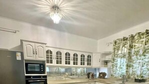 Une cuisine avec des meubles blancs, un réfrigérateur noir, un four encastré et un lustre.