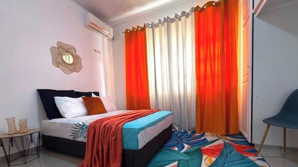 Une chambre à coucher moderne avec un lit, des rideaux colorés, un tapis à motifs et une petite table d’appoint.
