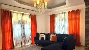 Un salon avec un canapé bleu foncé, un tapis à motifs et un lustre.