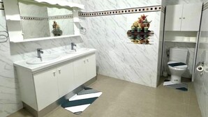 Une salle de bain avec un meuble-lavabo blanc, deux vasques, des toilettes et un miroir.