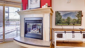 Una sala de estar con chimenea, televisor montado y ventana con persianas.