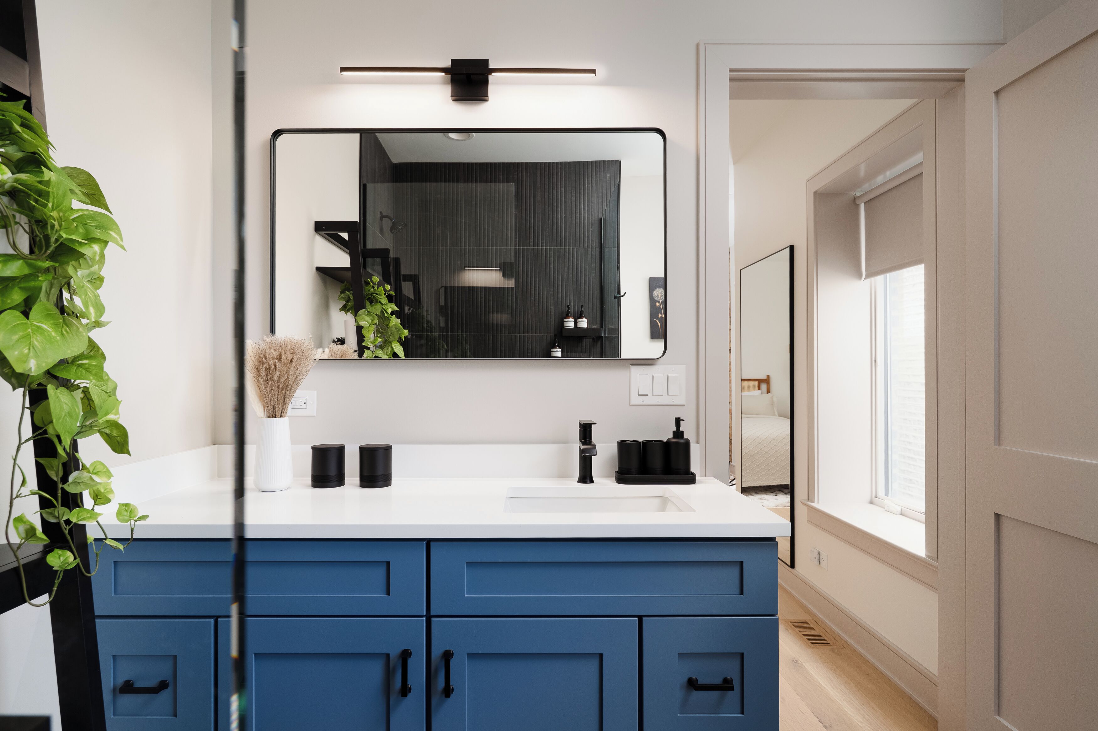 Un baño moderno con un tocador blanco, armarios azules, un espejo grande y una planta en maceta.