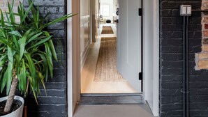 Un couloir avec un mur en briques noires, une plante en pot et une porte blanche donnant sur une autre pièce.