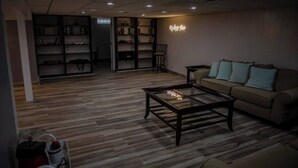 Una sala de estar con piso de madera, una mesa de centro de vidrio, un sofá con cojines y una estantería.