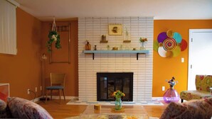Una sala de estar con chimenea, un estante azul y un colorido adorno en la pared.