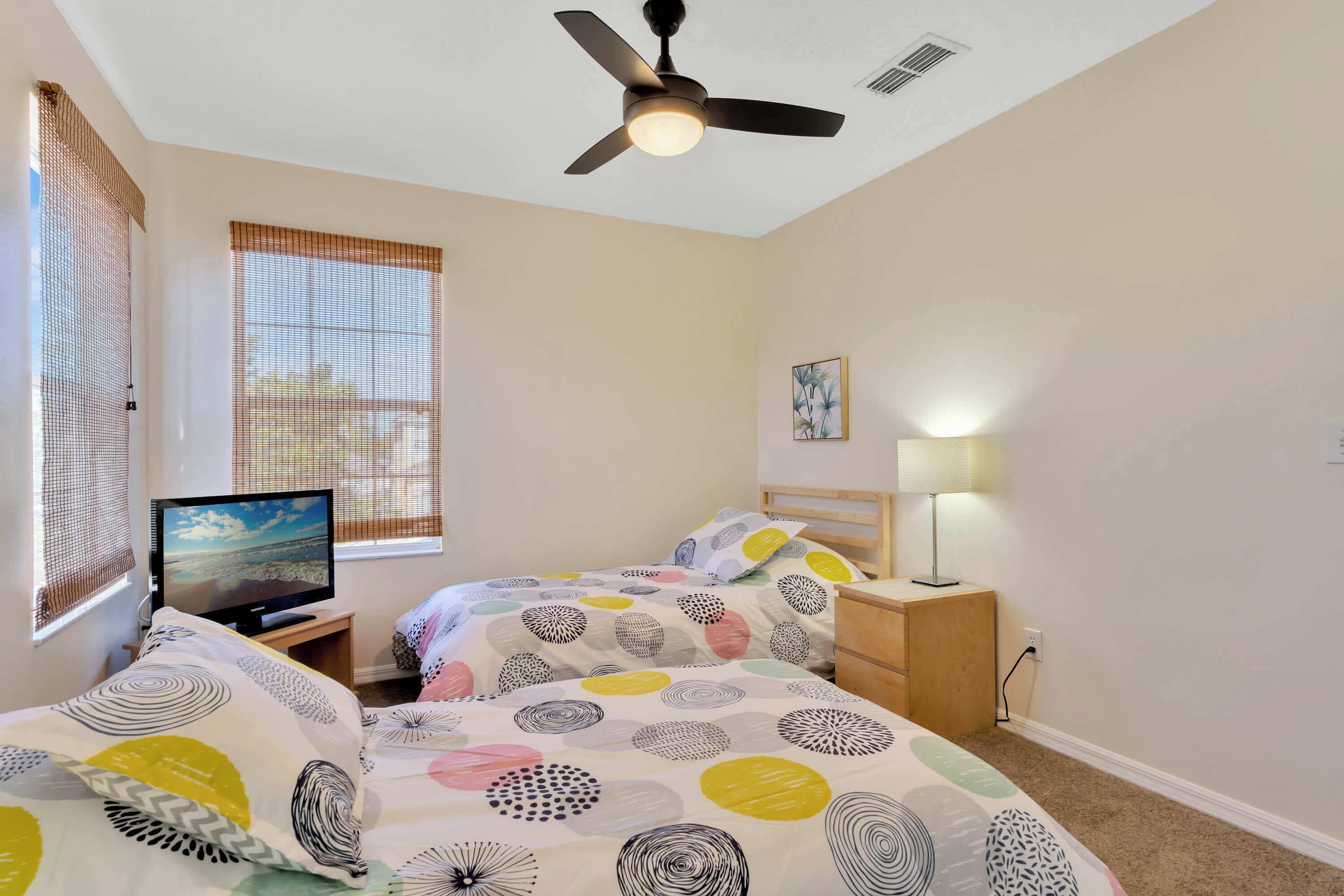 A bedroom with two beds, a ceiling fan, a TV, and a window with blinds.