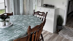 Et spiseområde med et bord dækket til to personer, træstole, et ur på væggen og et vindue med gardiner.