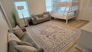 Et soveværelse med køjeseng, sofa, gulvtæppe med mønster og en loftslampe.