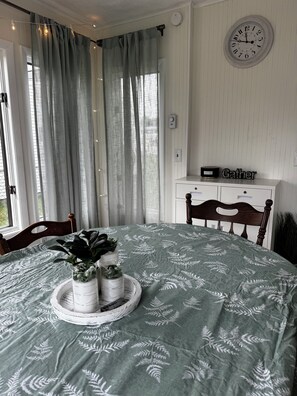 Quarto com uma cama, mesa de cabeceira com relógio, janela com cortinas e um aviso fixado na parede.