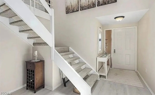 A staircase with a carpeted handrail, a small table with a lamp, and a door with a light fixture above it.