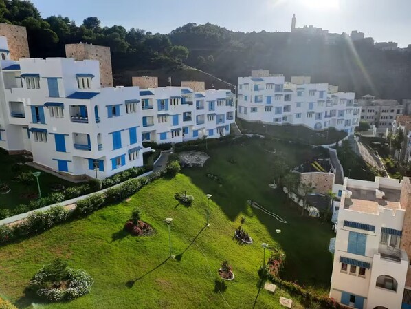 A residential area with modern buildings, a central green space, and a hill in the background. - Panoramic view | Cozy apartment M'diq (M'diq)