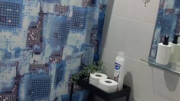 Une salle de bain avec un rideau de douche à motifs, un lavabo doté d’un distributeur de savon et un miroir reflétant les articles de toilette.