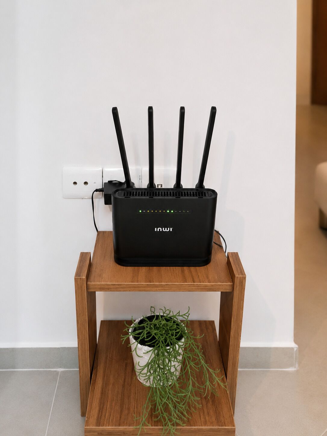 A black router with multiple antennas on a wooden side table against a white wall.