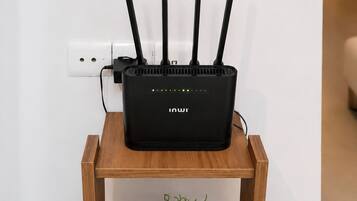 A black router with multiple antennas on a wooden side table against a white wall.