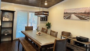 Un coin repas avec une table et des chaises en bois, un luminaire suspendu et un tableau au mur.