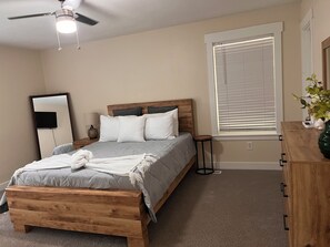 A bedroom with a bed, a wooden dresser, a mirror, a ceiling fan, and a window with blinds. - 3-bedroom house in peaceful Norcross with cool AC (Norcross)
