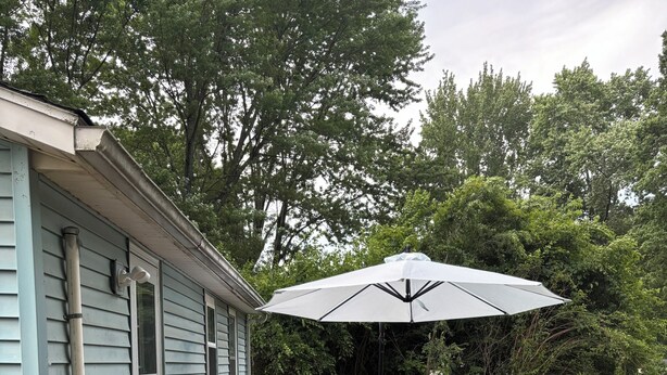 Une terrasse en bois avec une table et des chaises, un parasol et un grand pot de fleurs.