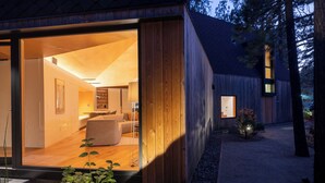 Une cabane moderne en bois, dotée d’un intérieur ouvert, d’un espace de vie bien visible et d’un éclairage extérieur soigné.