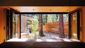 Un intérieur moderne avec un plancher en bois, une porte vitrée donnant sur un espace extérieur agrémenté d’arbres et d’une clôture en bois.