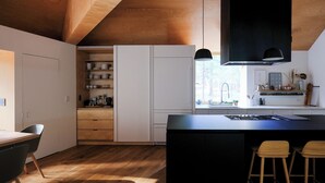 Une cuisine moderne avec un plancher en bois, des meubles blancs, un îlot central noir et des luminaires suspendus.