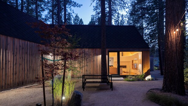 Une cabane moderne avec une façade en bois, une allée en gravier et un banc.