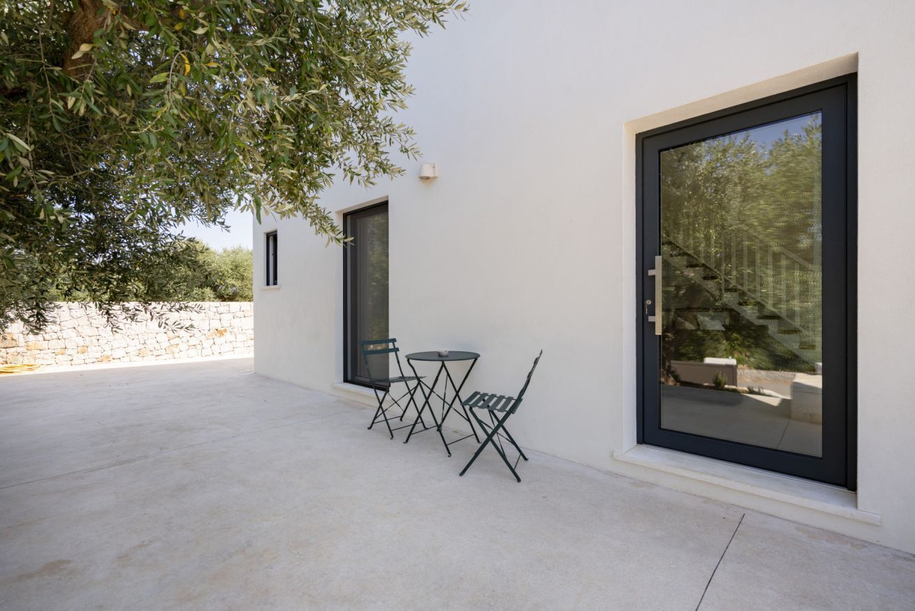 A patio with a table and chairs, a large window, and a tree.
