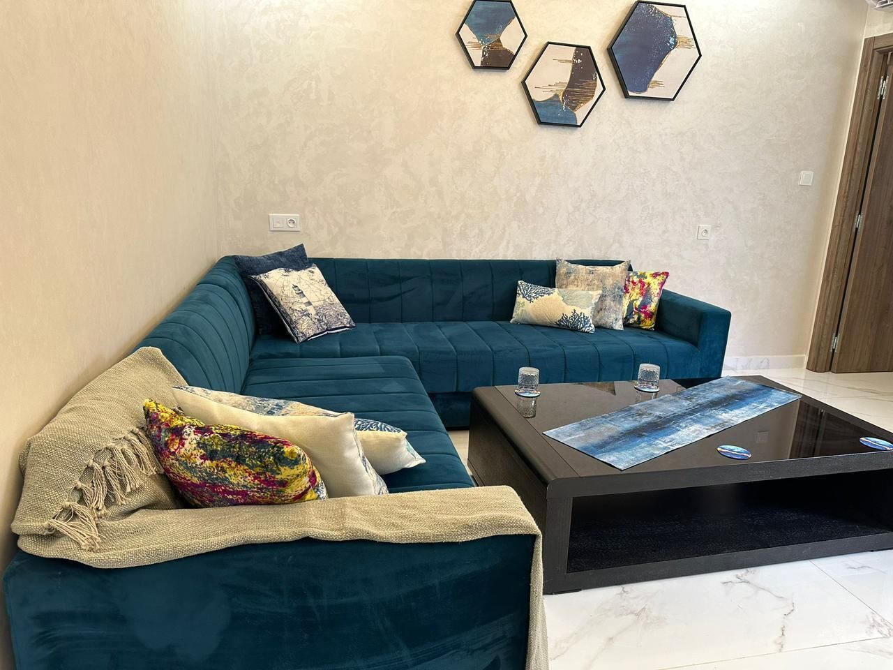 Un salón con un sofá turquesa, una mesa de centro de vidrio y decoración mural hexagonal.