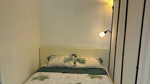Un lit simple avec une couvre-lit à motifs floraux, une lampe de chevet et un rideau.