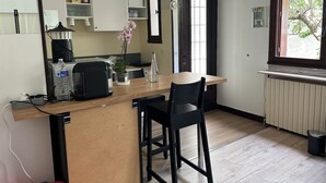 Une cuisine compacte dotée d’un plan de travail en bois, de deux tabourets de bar noirs, d’une machine à café et d’une orchidée en pot.