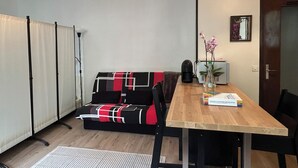 Une petite pièce chaleureuse, avec une table à manger en bois, un canapé noir et rouge, un petit tapis blanc et un luminaire suspendu au plafond.