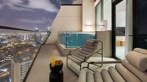 Un balcón moderno con piscina de cristal, una silla de descanso y una mesa con alimentos para el desayuno.