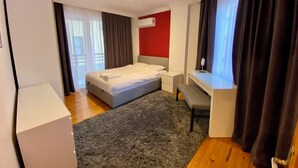 Ein Hotelzimmer mit Bett, Nachttisch, Schreibtisch und einem fenster mit Vorhängen.