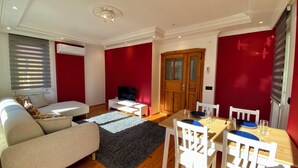 Ein Wohnzimmer mit Sofa, Fernseher und Esstisch mit Stühlen.