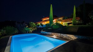 A modern house with a swimming pool, stone walls, and tall trees.