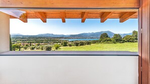 A balcony with a wooden ceiling and a view of a lake, mountains, and a town.