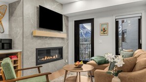 Ein modernes Wohnzimmer mit Kamin, einem an der Wand befestigten Flachbildfernseher, einer gemütlichen Couch und einem Essbereich mit Tisch.