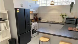Una cocina moderna con armarios blancos, un refrigerador negro, una estufa y dos taburetes de madera.