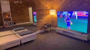 Una habitación con pared de ladrillo, un televisor y dos sofás blancos.