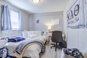 A bedroom with a bed, a desk, a chair, a calendar, and a wall with a sign.
