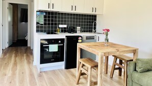 Eine moderne Küche mit weißen Schränken, einer schwarzen Spritzschutzwand, Bosch-Geräten und einem Holztisch mit einem grünen Kissen.